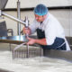 Male-presenting person in a cheese factory setting using machinery to stir a vat of liquid.