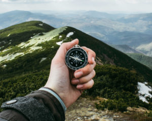 Mountain scape with a hand holding out a compass toward the mountain top