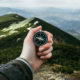 Mountain scape with a hand holding out a compass toward the mountain top